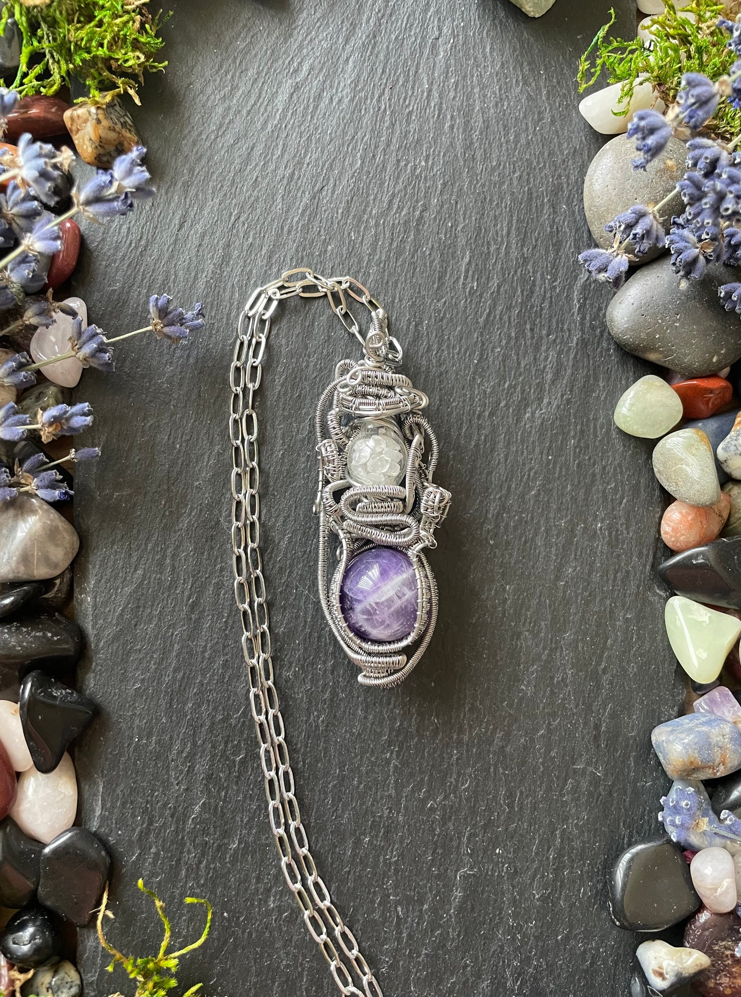 A crystal ball amulet in stainless steel wire with purple amethyst sphere, and a glass vial filled with clear quartz crystals