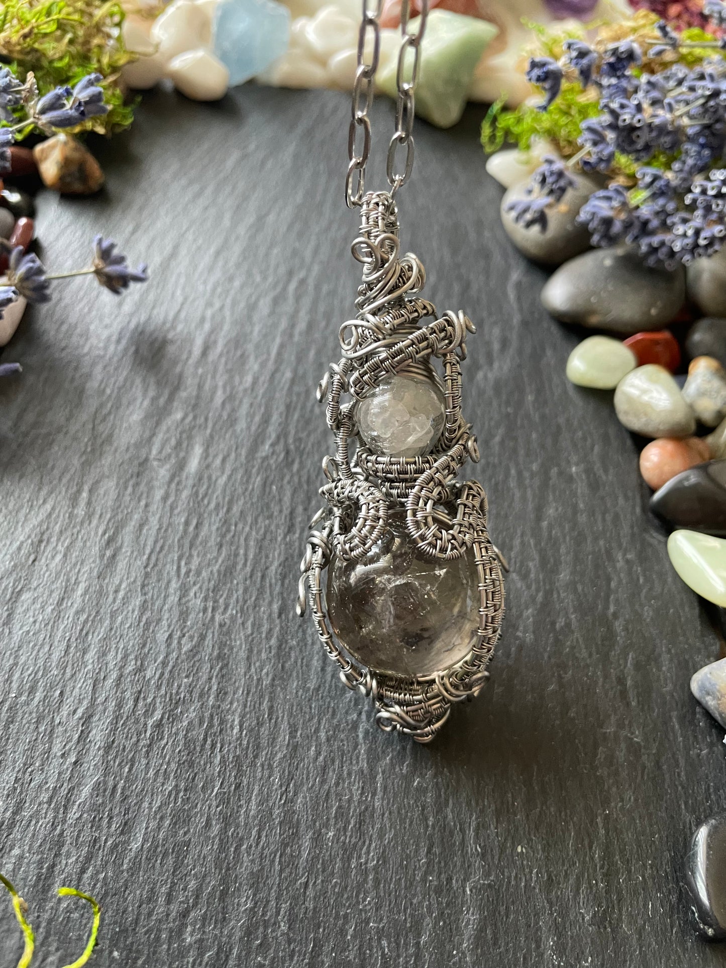 A magic crystal ball amulet with a smoky quartz sphere and glass vial filled with clear quartz, in stainless steel wire wrap