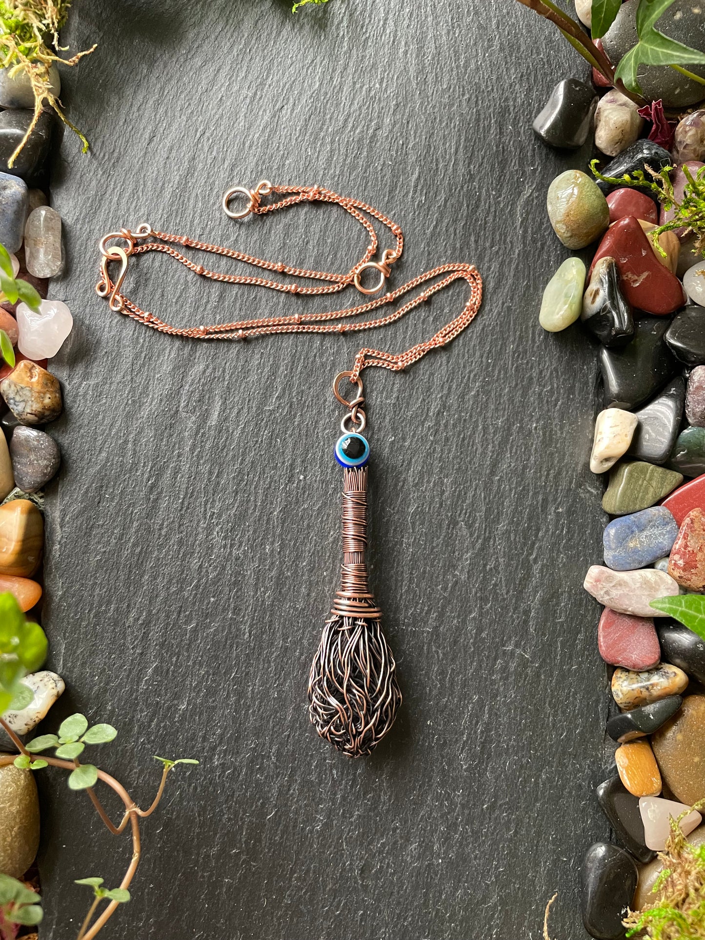 Necklace with a unique pendant on a dark stone surface with pebbles and plants around
