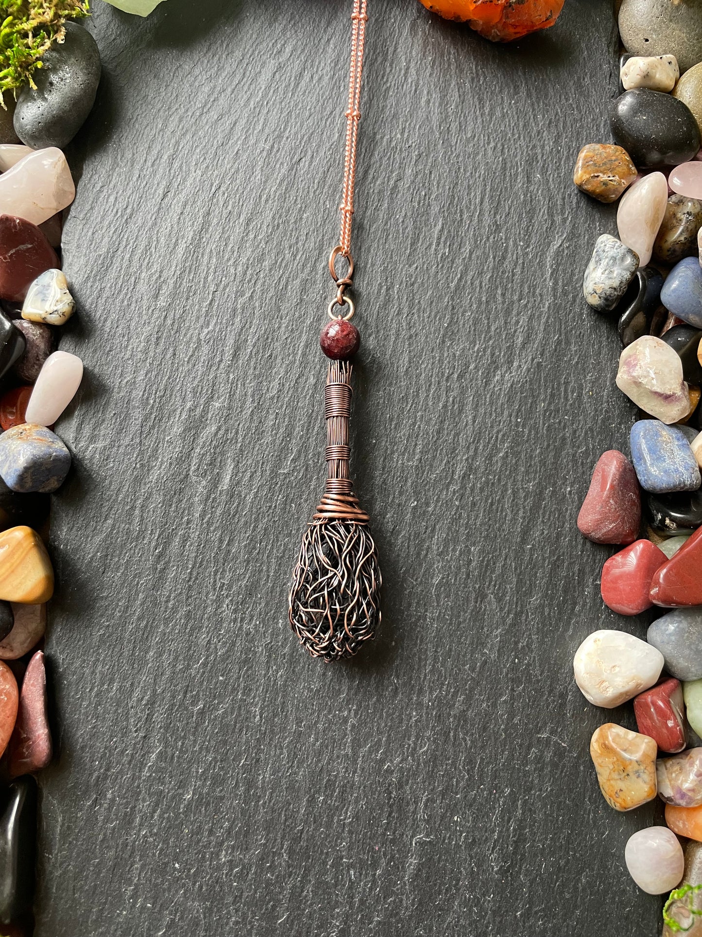 Decorative broom on a dark stone surface with colorful stones around