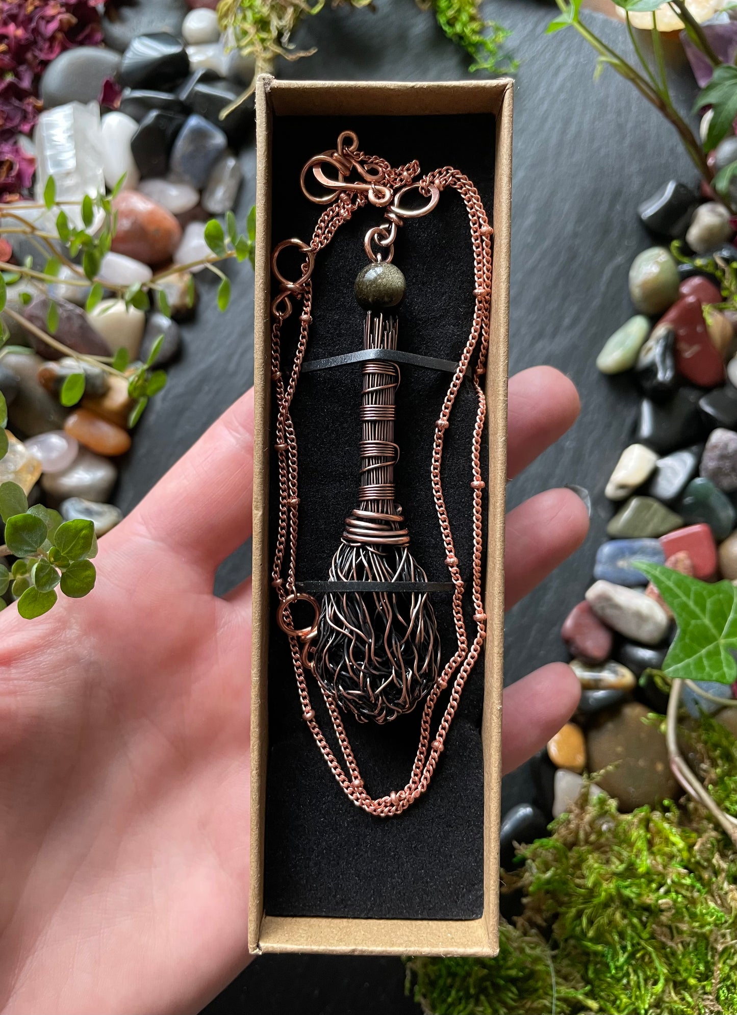 Copper necklace in a box held by a hand with a natural stone background