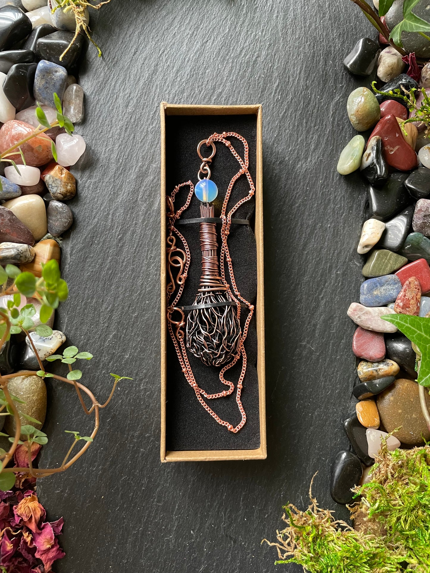 Decorative item in a box on a stone surface with stones and plants around