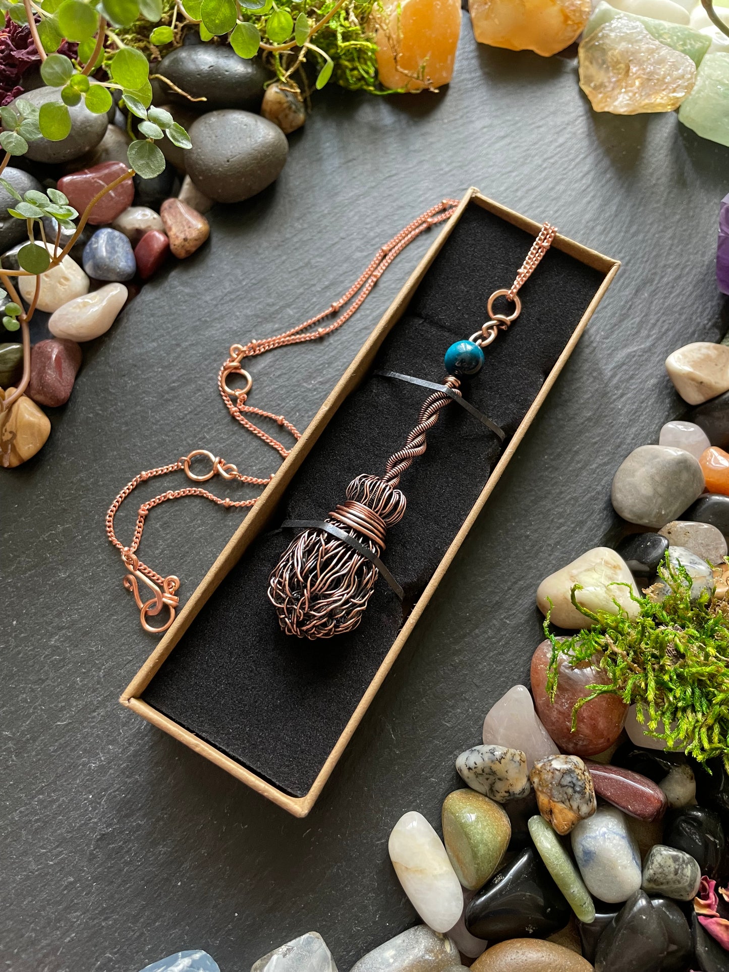 Necklace with a decorative pendant in a box surrounded by stones and plants