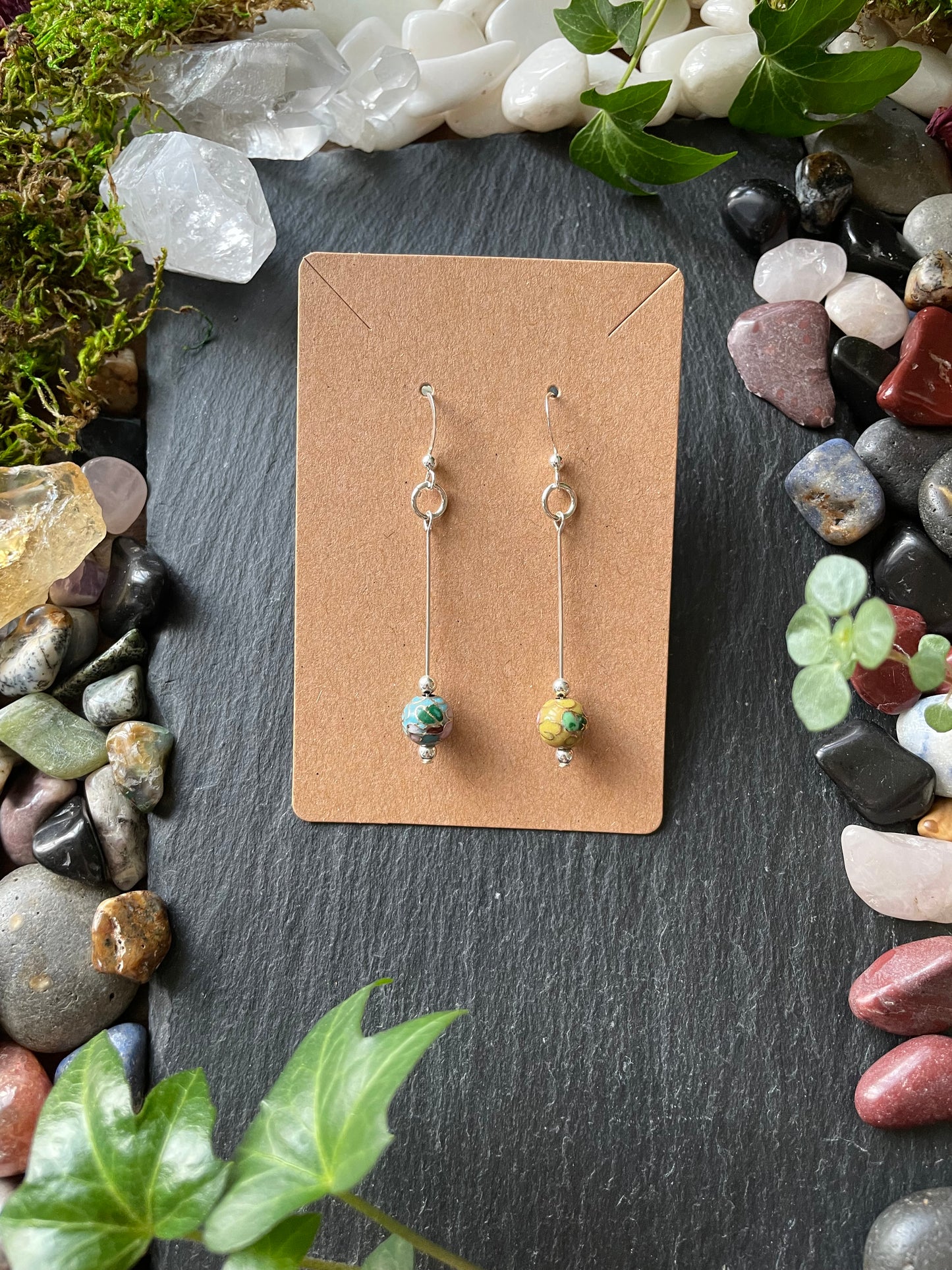Three small earrings on a brown card with a natural stone and plant background