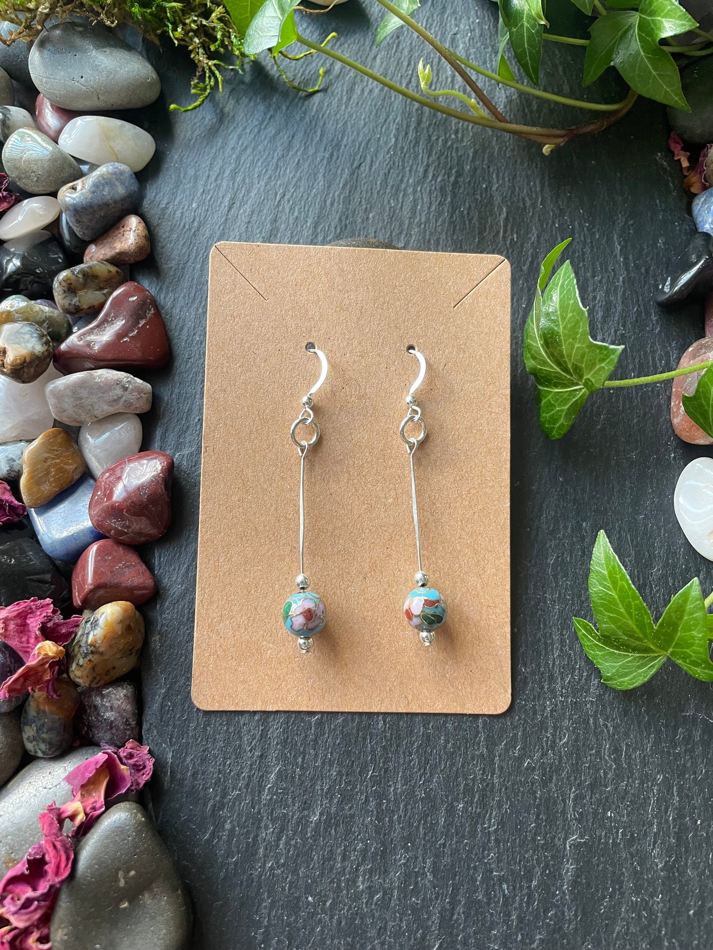 Pair of earrings on a cardboard backing with pebbles and plants around