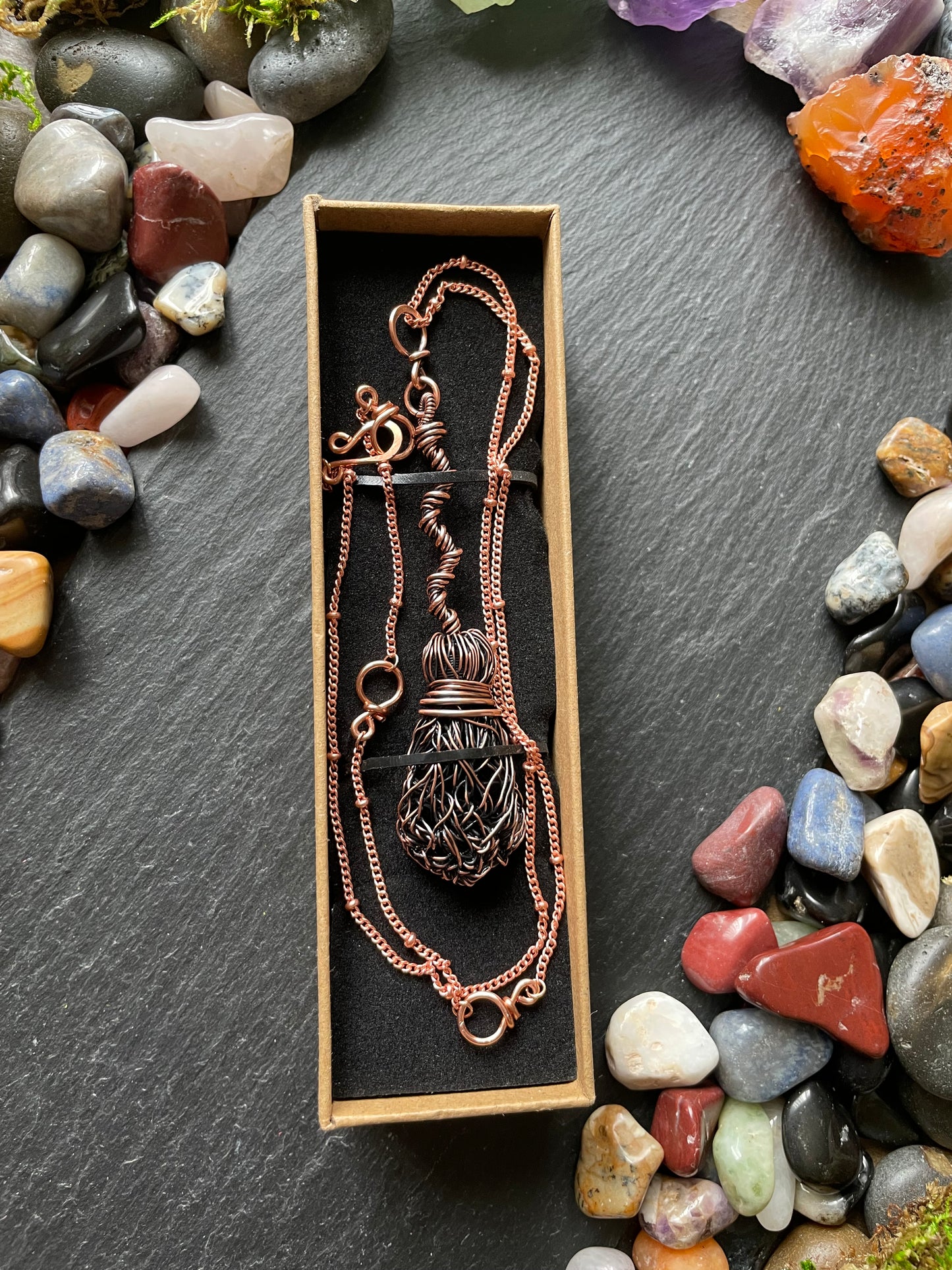 Necklace in a box surrounded by colorful stones on a dark surface