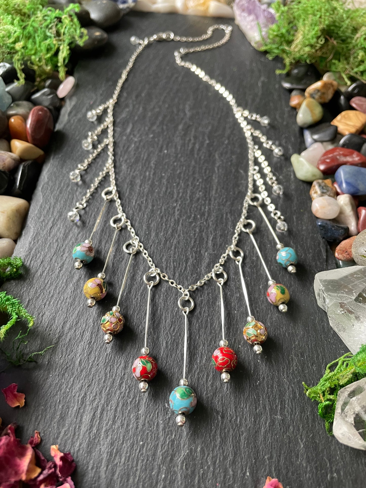 Necklace with colorful beads on a dark stone surface with stones and moss around