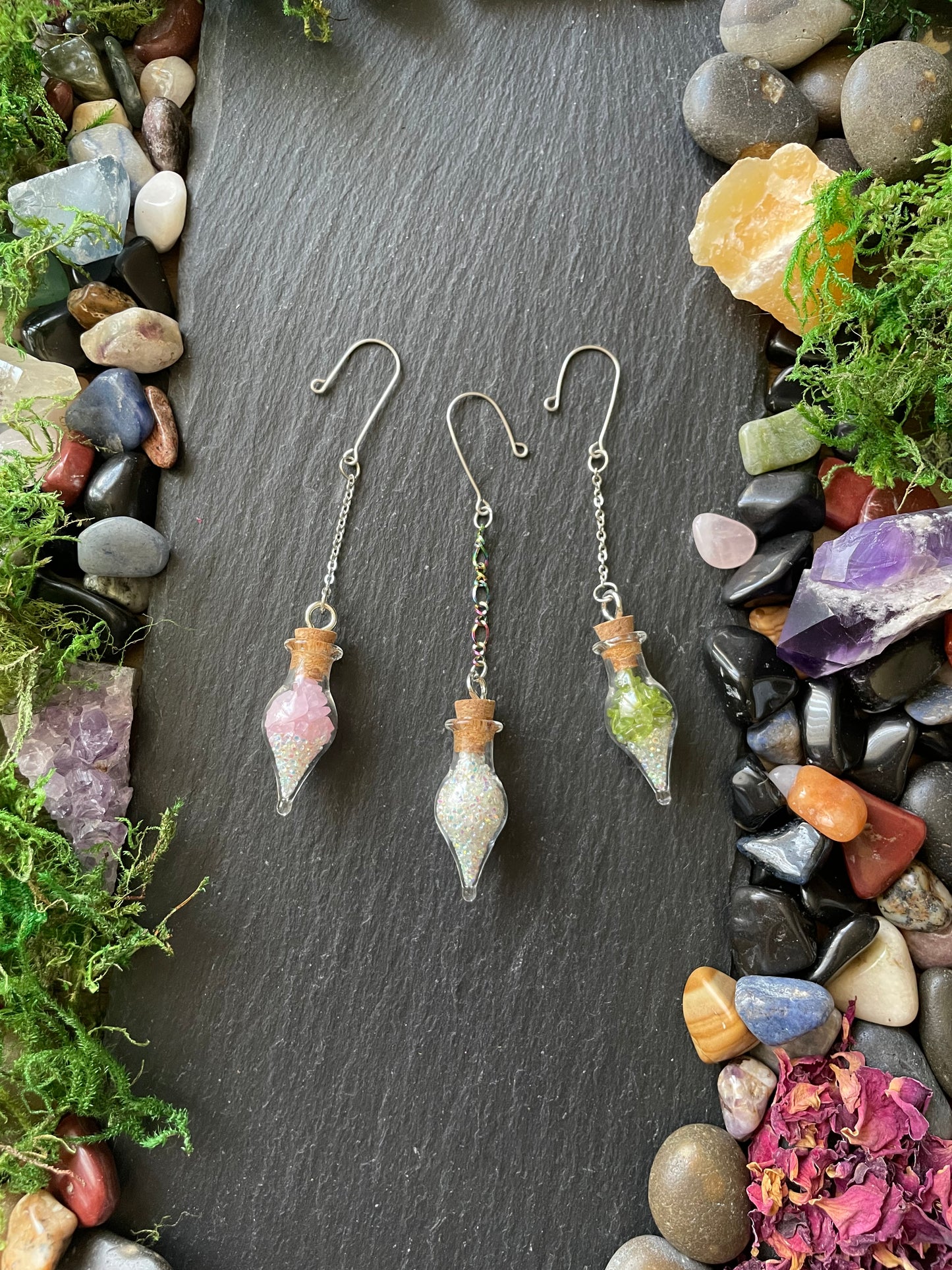 Crystal plant charms on a dark stone surface with stones and moss around