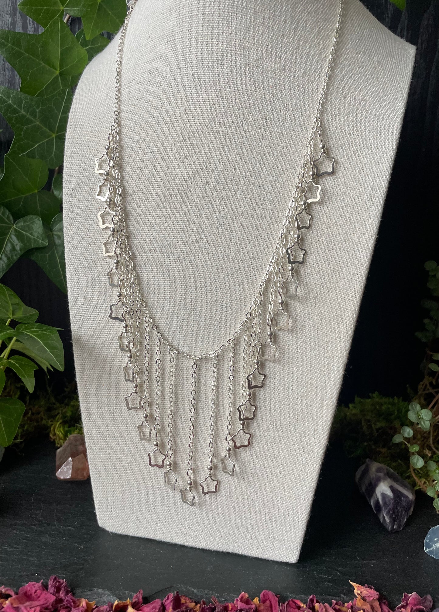 Silver necklace with star-shaped charms on a mannequin bust against a natural background.