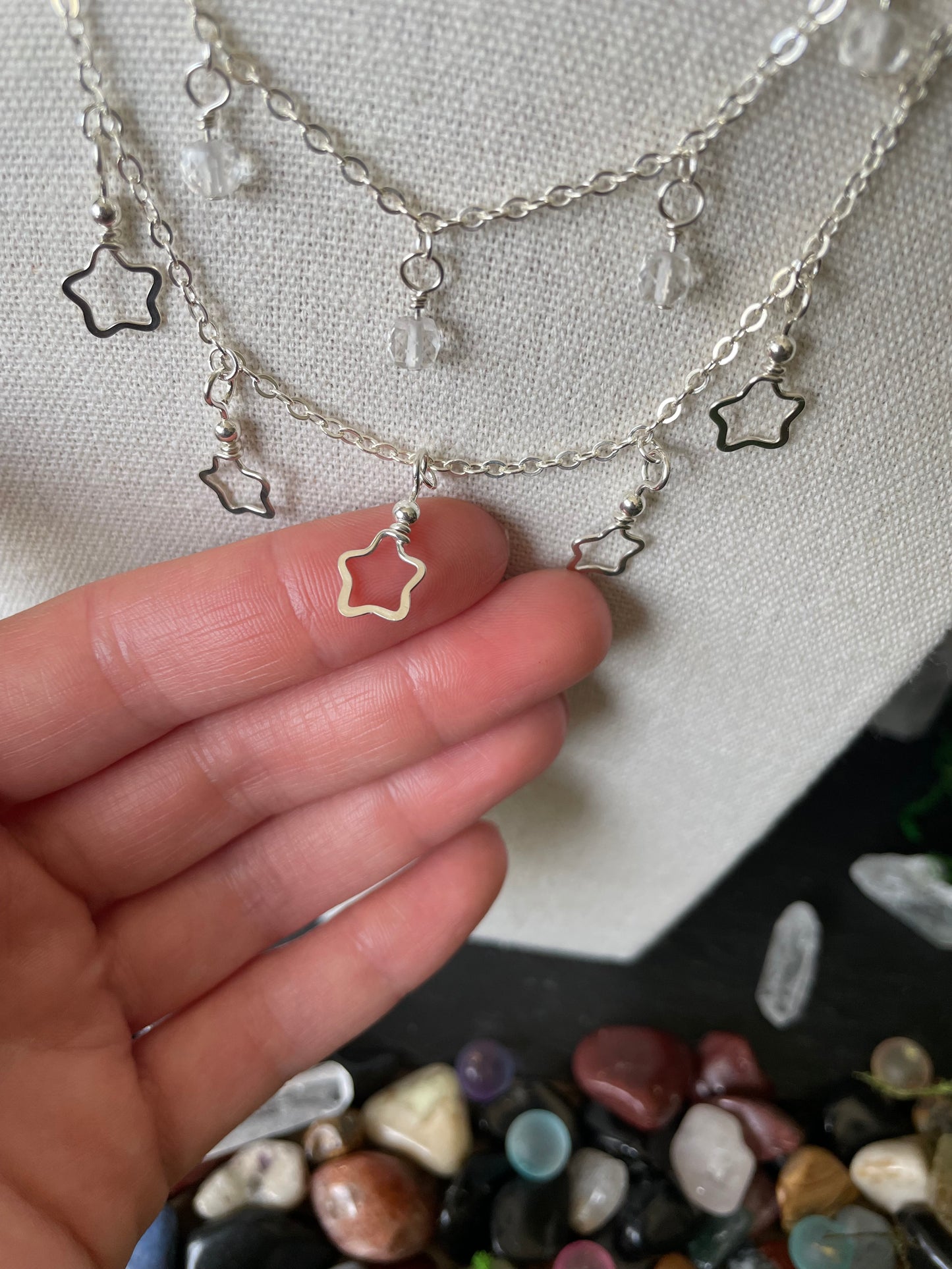 Close-up of a hand holding a silver star necklace charm on a textured fabric background.
