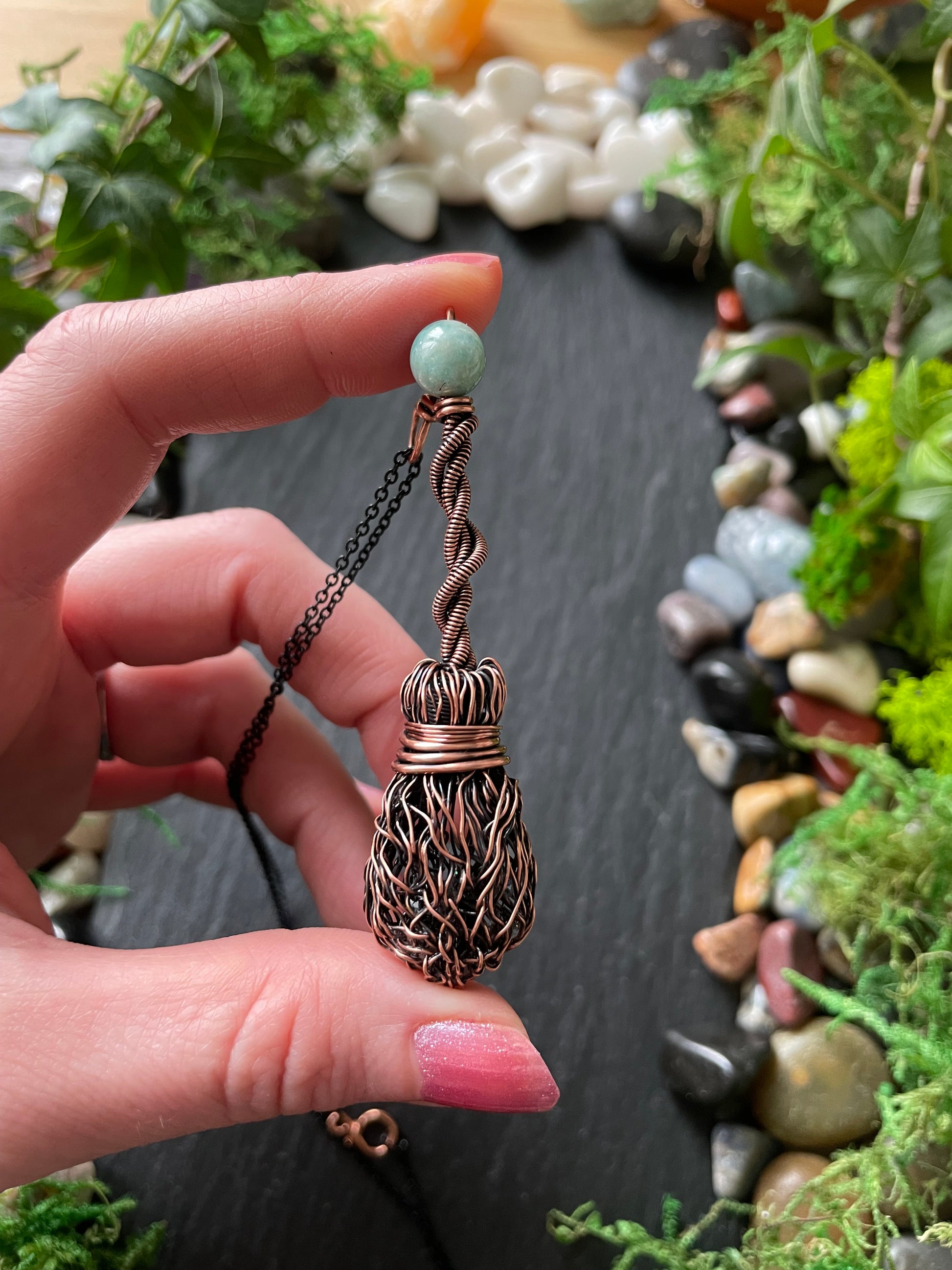 Hand holding a decorative mini wire broom with a natural stone background