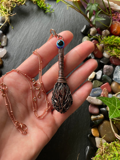 Hand holding a copper necklace with a decorative pendant against a natural stone and moss background