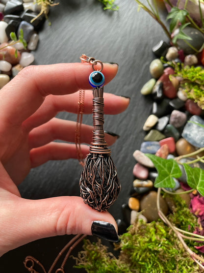 Hand holding a decorative broom with an eye design against a natural stone and moss background