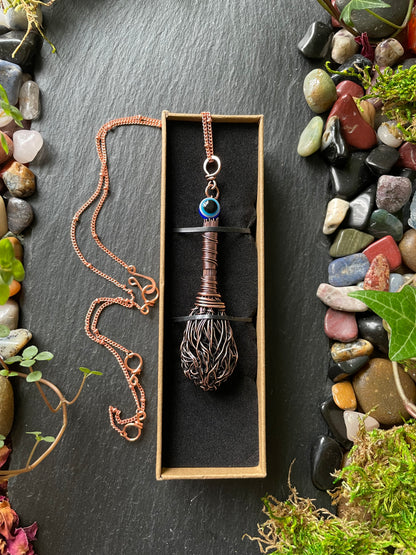 Necklace with a decorative pendant in a box on a dark surface with stones and plants.