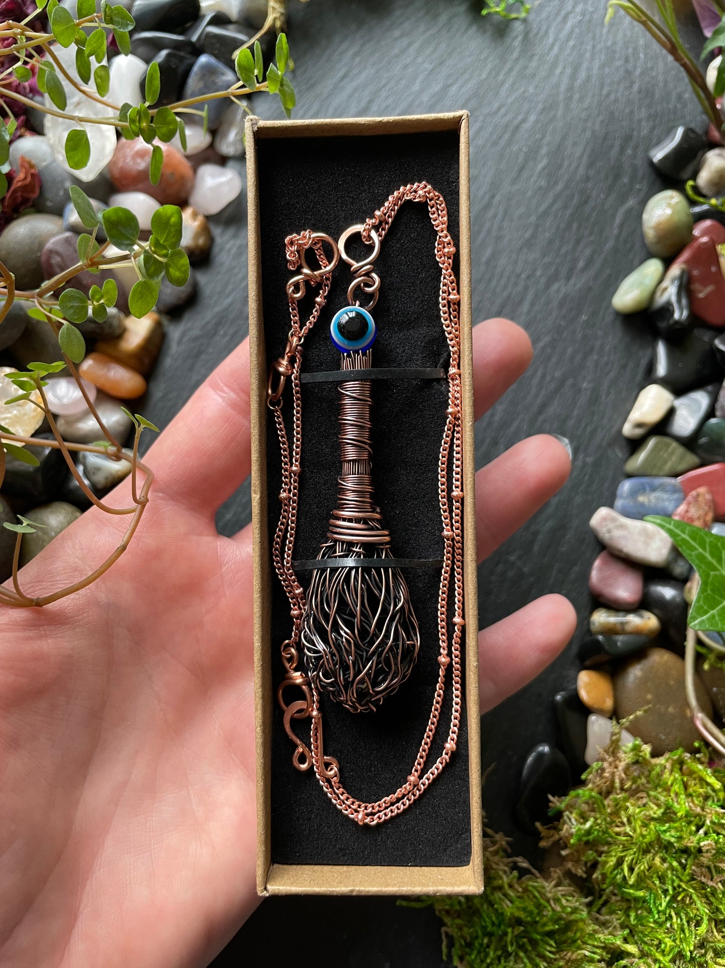 Hand holding a decorative necklace in a box with a natural stone and moss background