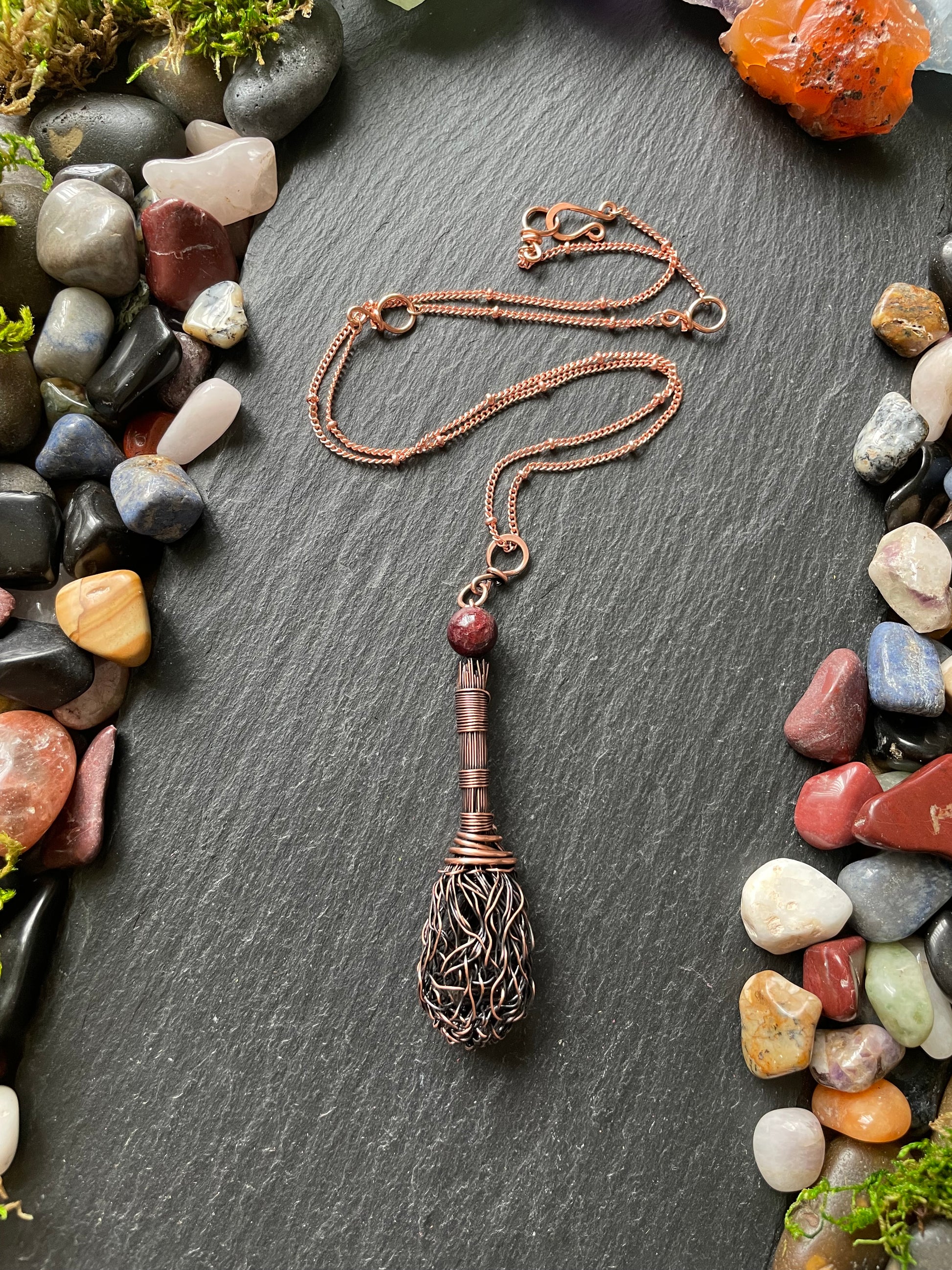 Necklace with a broom on a dark surface surrounded by multicolored stones
