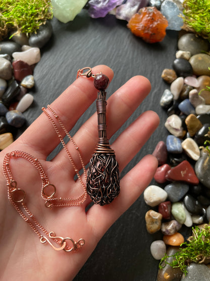 Hand holding a copper-colored broom necklace with pebbles and moss in the background