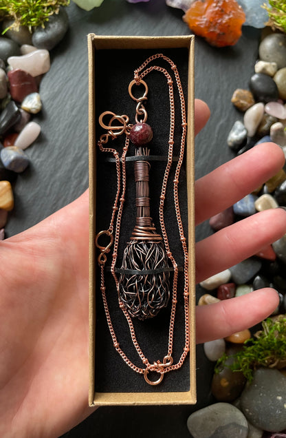 Copper necklace with intricate design held in a hand against a natural stone background