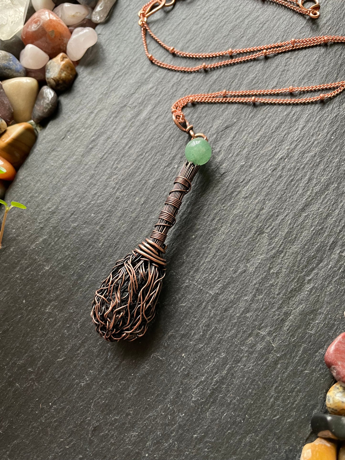 Decorative broom with a green bead on a dark surface with pebbles