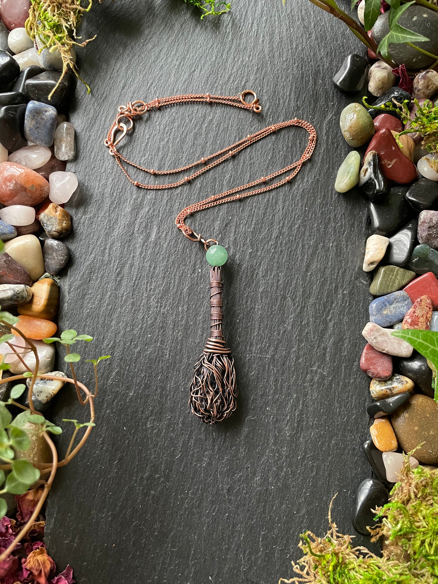 Necklace with a unique pendant on a dark slate surface surrounded by pebbles and plants