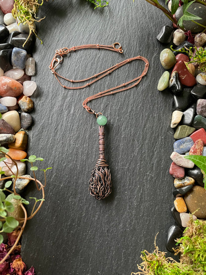 Necklace with a unique pendant on a dark slate surface surrounded by pebbles and plants