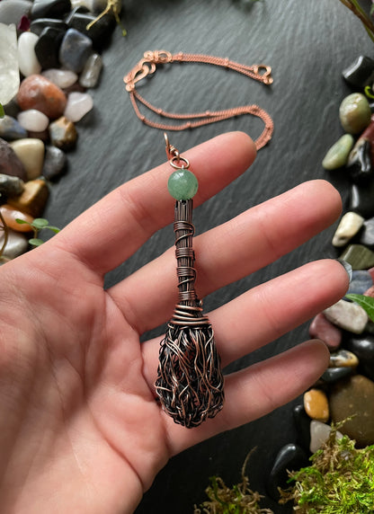 Hand holding a decorative pendant with a green bead against a natural stone background