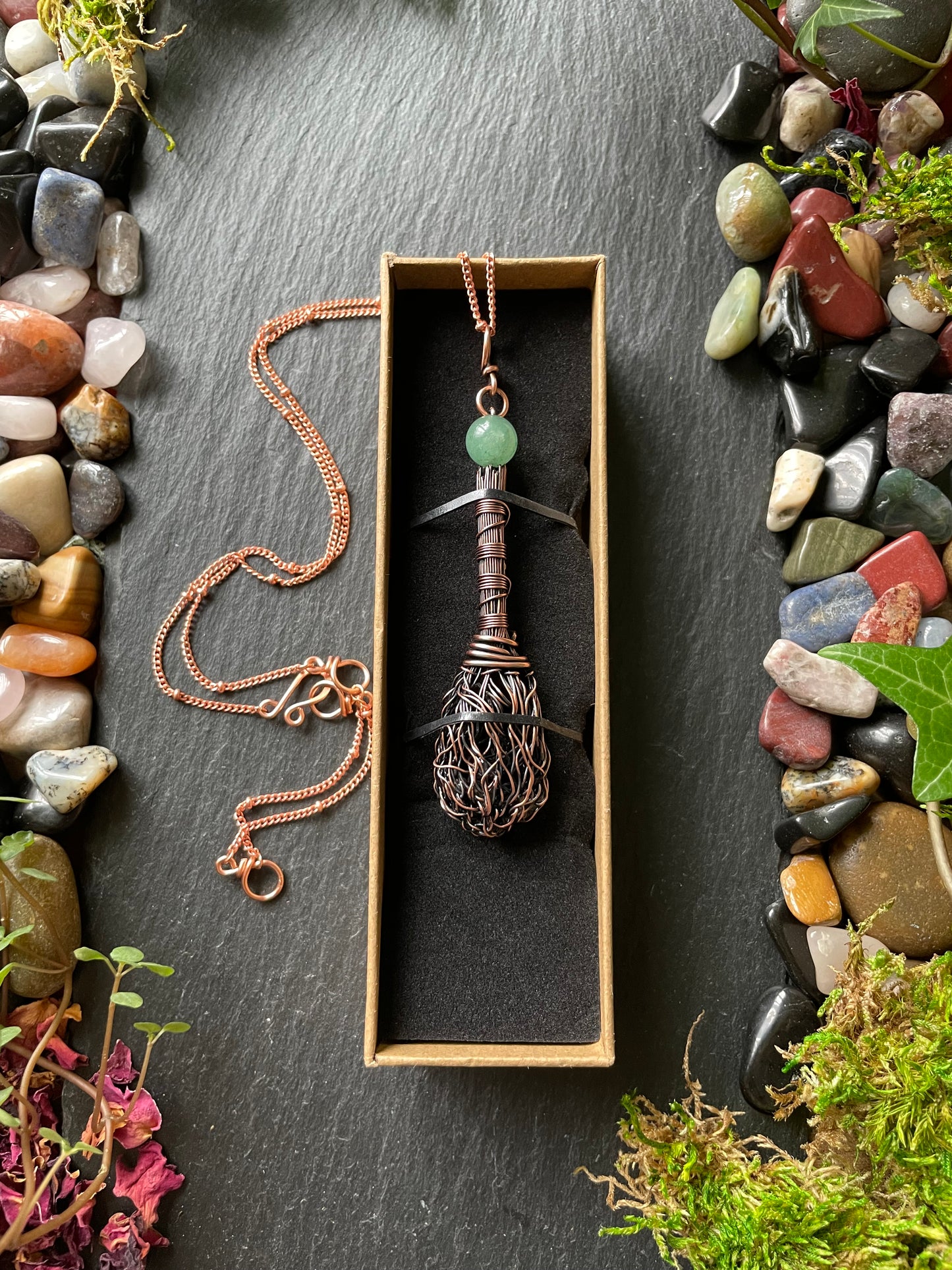 Necklace with a decorative pendant in a box on a stone surface with moss