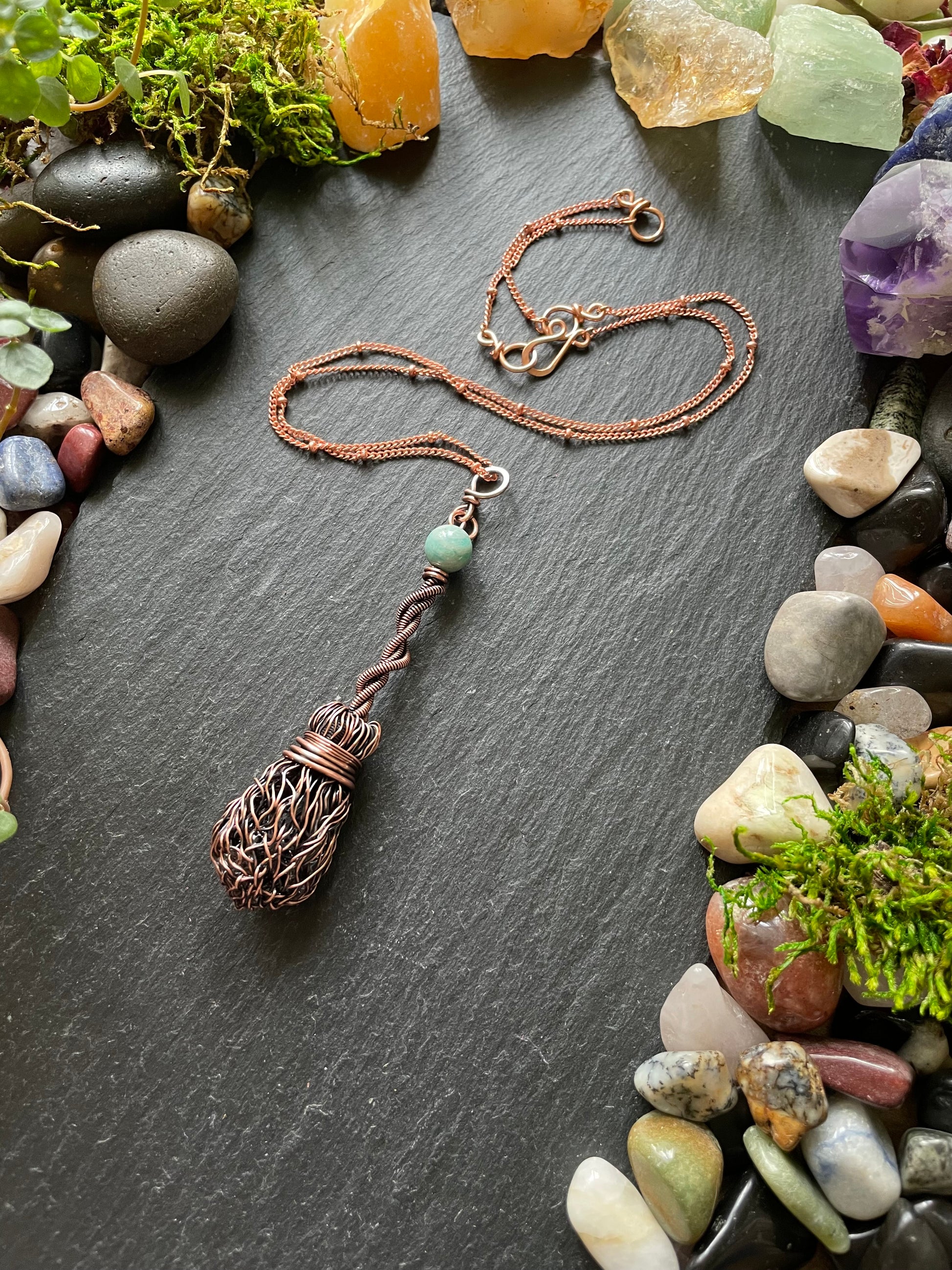 Copper necklace with a decorative pendant on a dark surface surrounded by stones and crystals