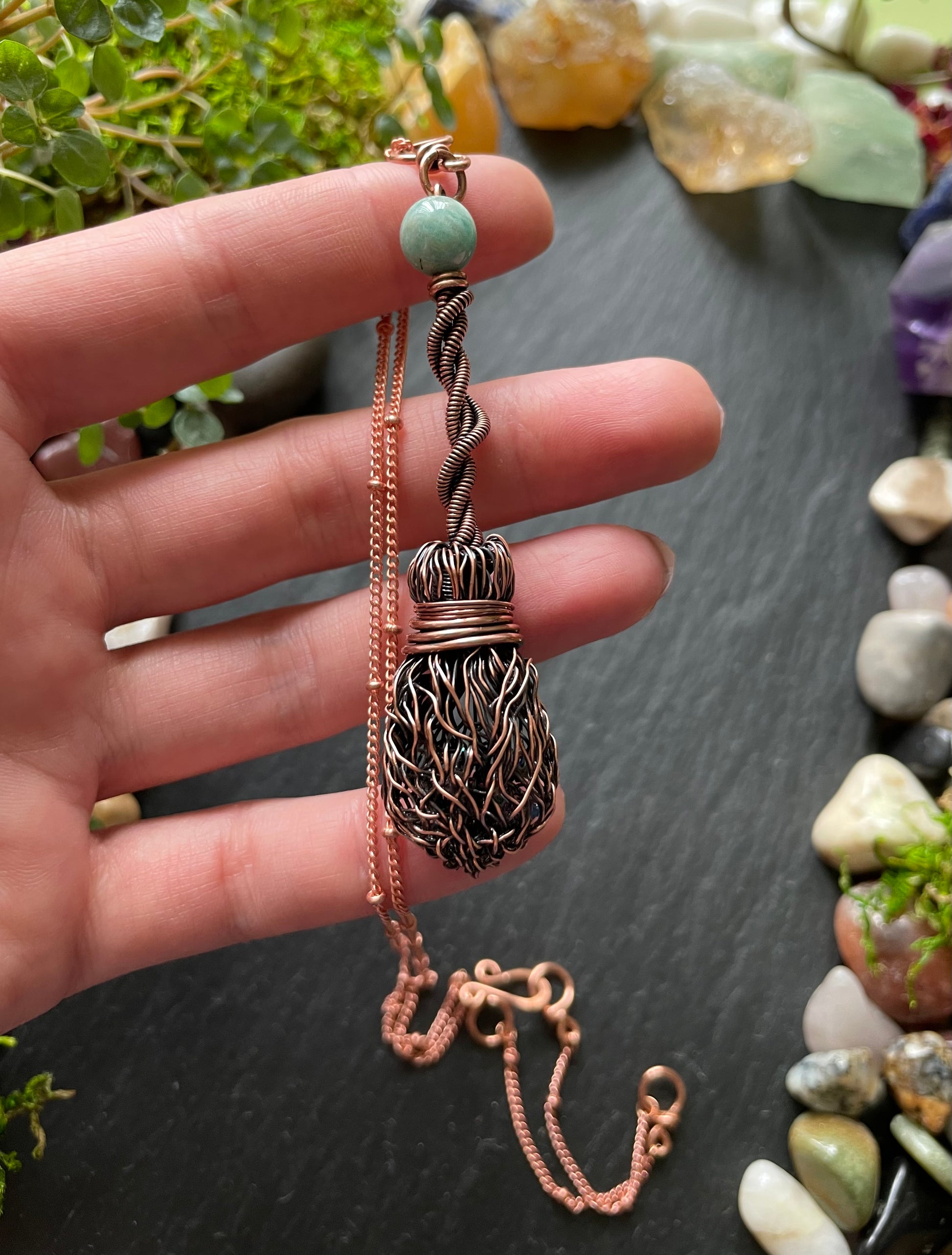 Hand holding a decorative necklace with a detailed pendant against a natural stone background