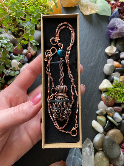 Copper necklace in a box held by a hand with a natural stone background