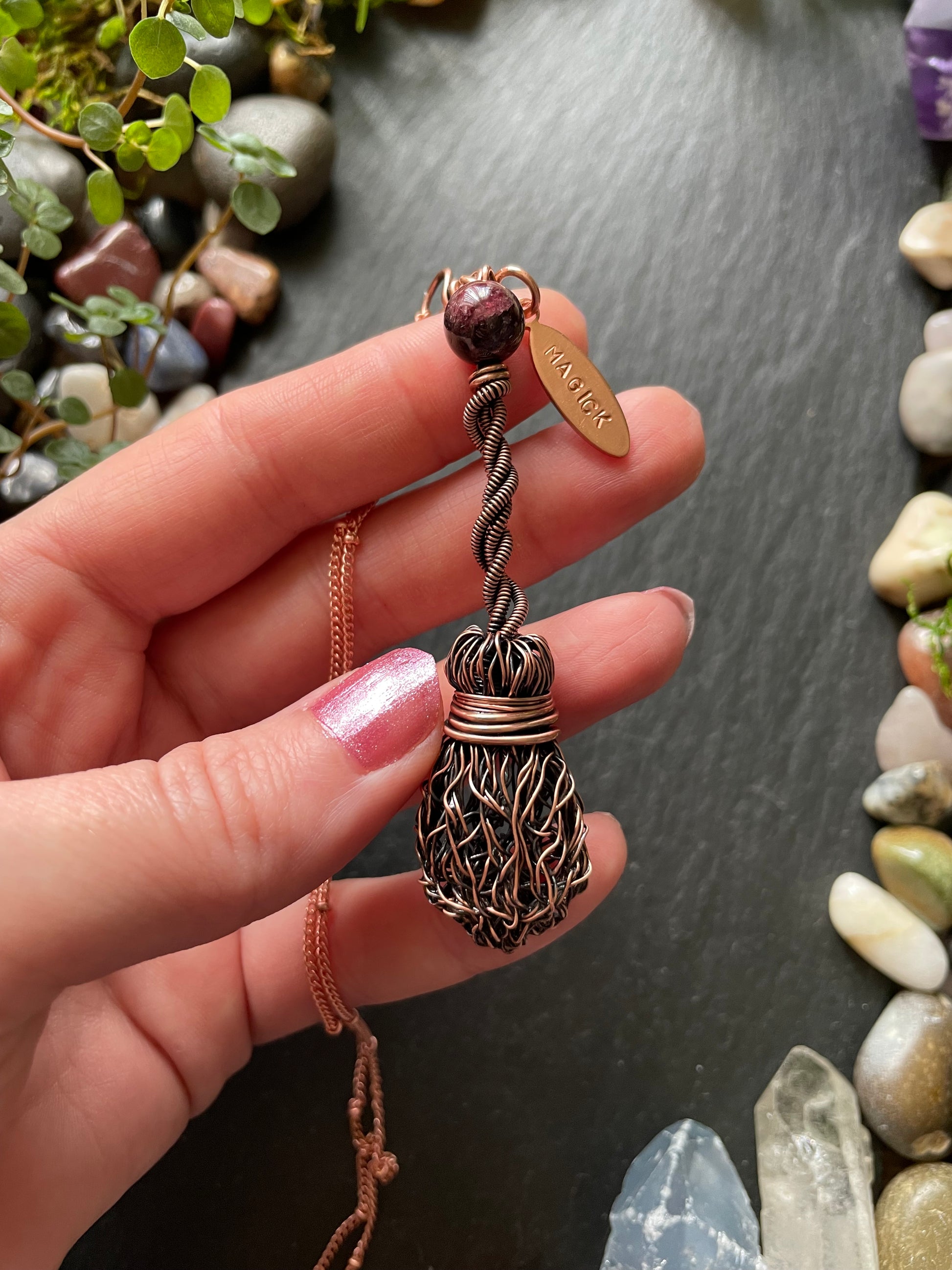 Hand holding a copper necklace against a stone background