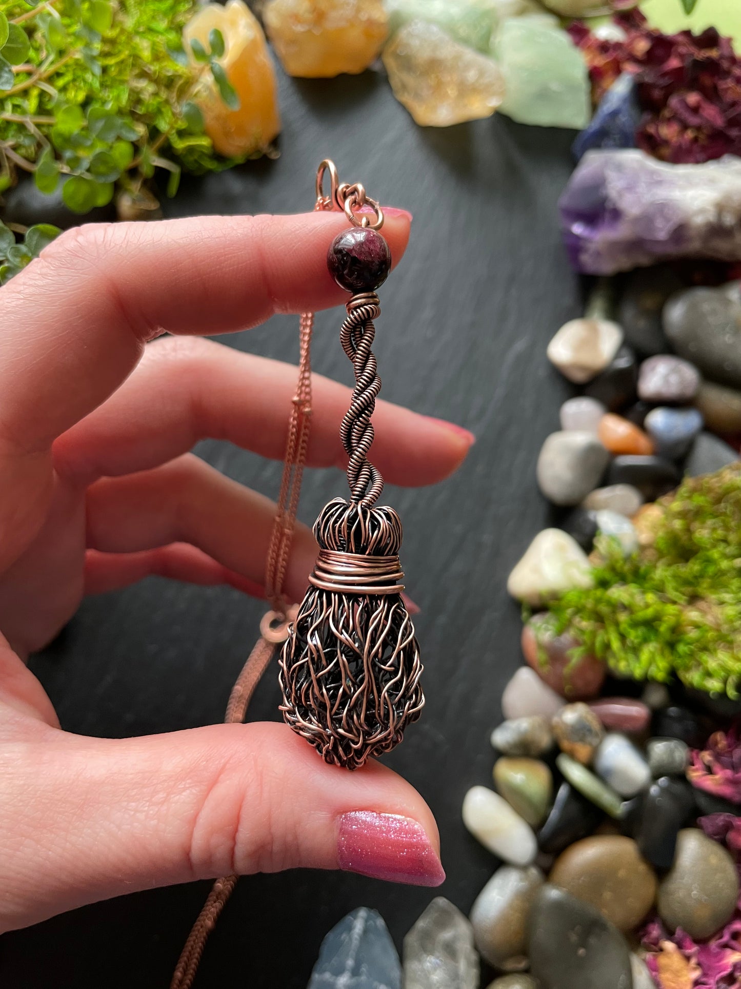 Hand holding a decorative necklace with a natural stone and moss background