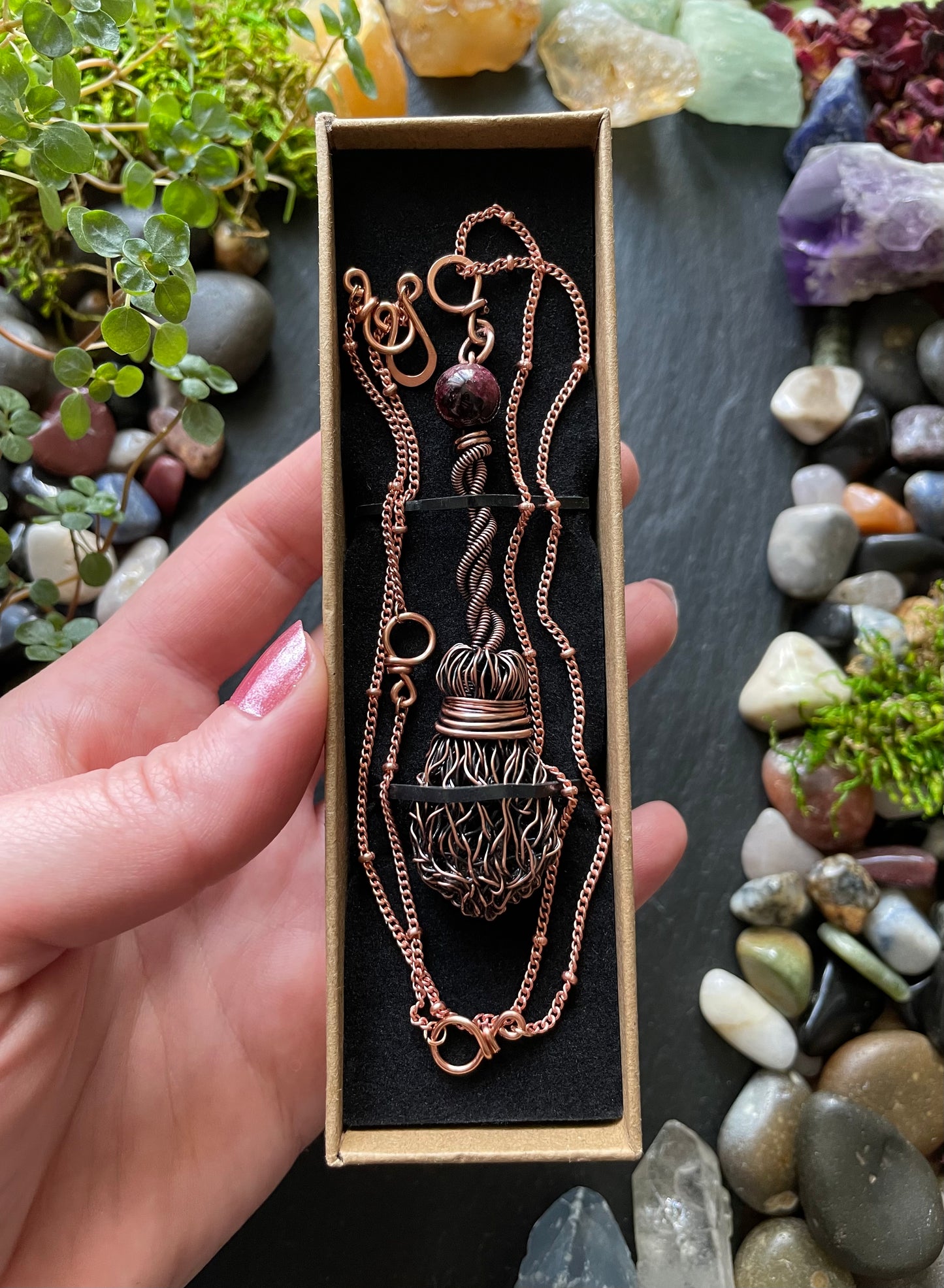 Copper necklace in a box held by a hand with a natural stone background