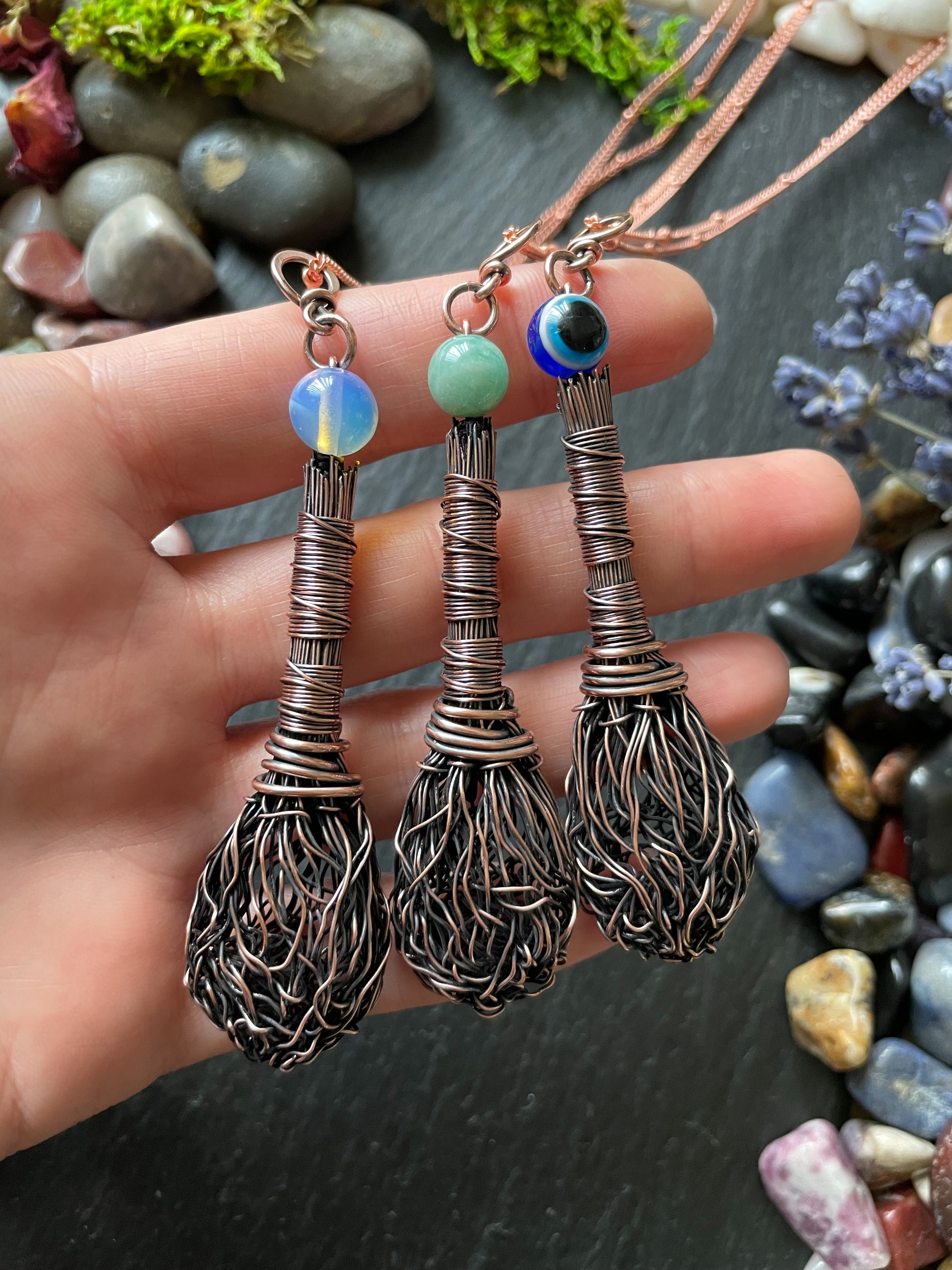 Three miniature copper wire broom pendants with opalite, amazonite, and evil eye bead displayed in hand