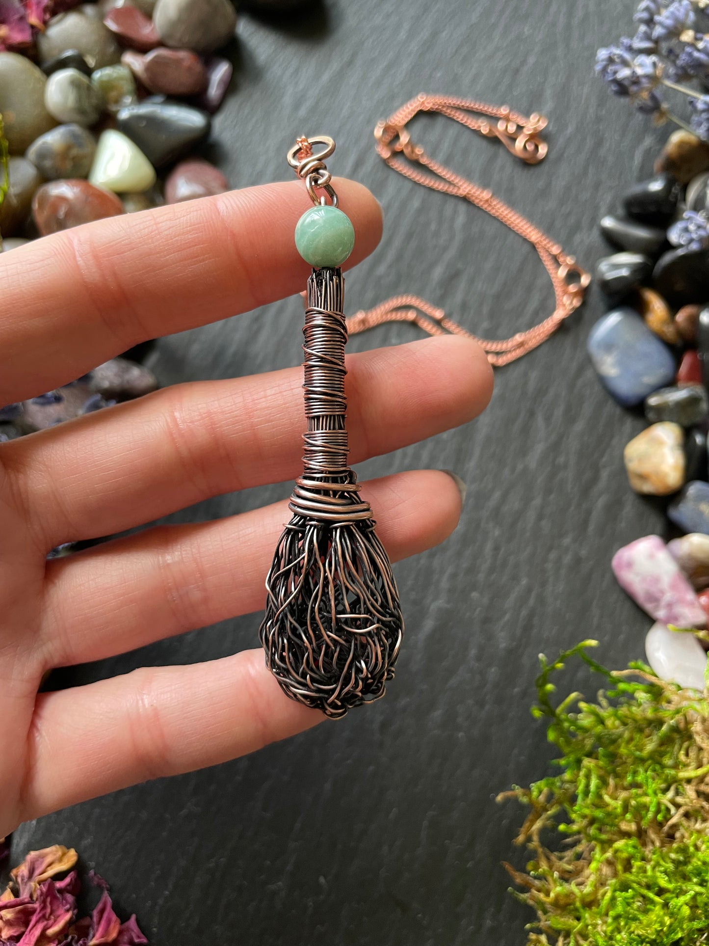 Miniature wire broom pendant with an amazonite crystal bead topper, attached to a copper chain and held in hand