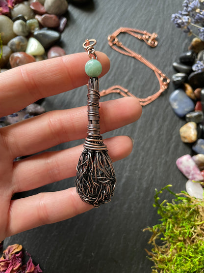 Miniature wire broom pendant with an amazonite crystal bead topper, attached to a copper chain and held in hand