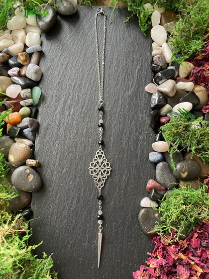 Silver car mirror charms on a dark slate surface surrounded by stones and plants