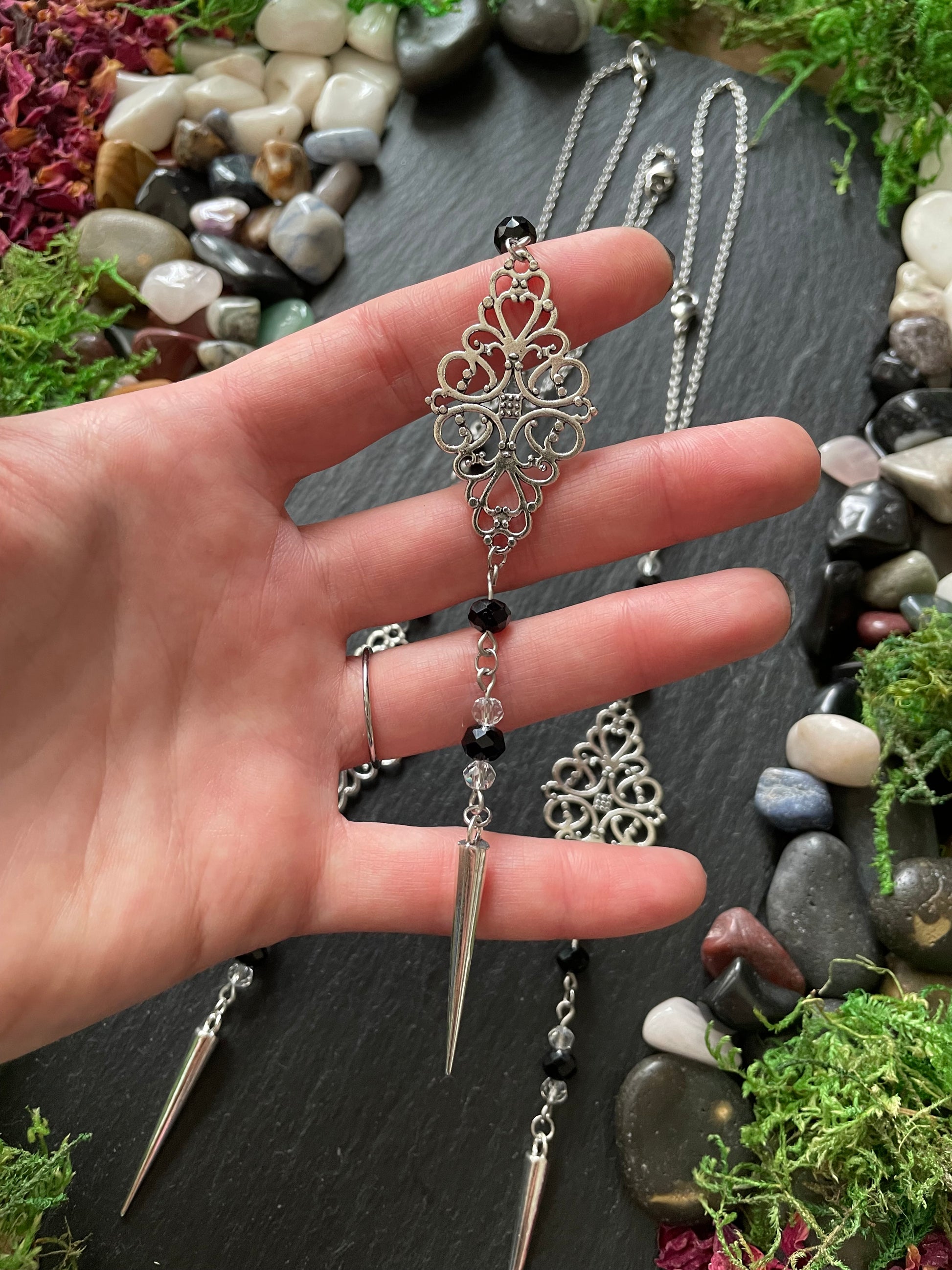 Hand holding a silver car mirror charm with intricate design against a natural stone background