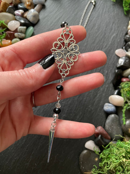 Hand holding a decorative car mirror charm with intricate design against a natural stone background