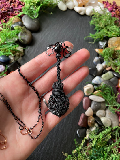 A hand holding a black broom pendant with celestial charms.