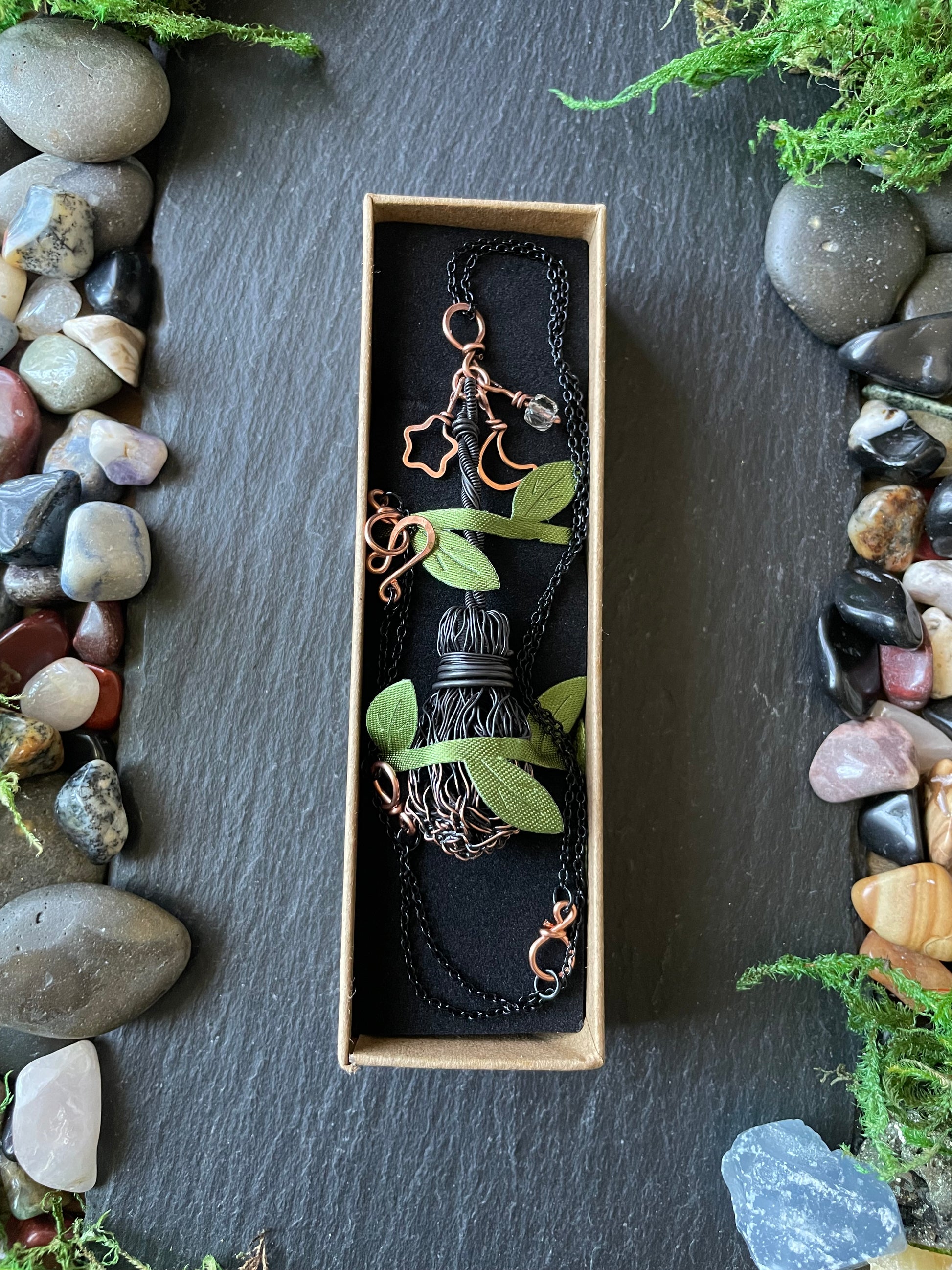 Broom pendant in a box with stones and plants around