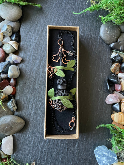 Broom pendant in a box with stones and plants around