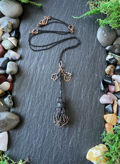 Necklace with a decorative pendant on a dark surface surrounded by stones and plants