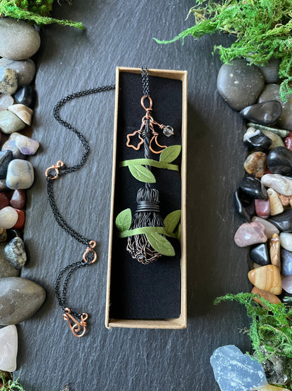 Necklace with handmade broom pendant in a box on a stone and moss background