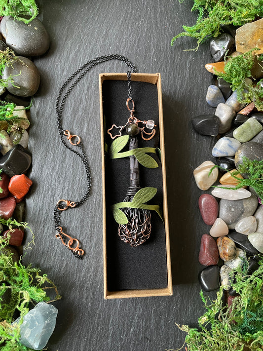 A mini wire broom pendant in box  surrounded by decorative moss and river stones.