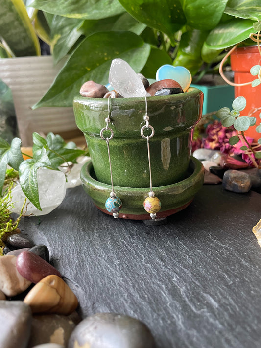 Green ceramic pot with earrings on a dark surface surrounded by plants and stones