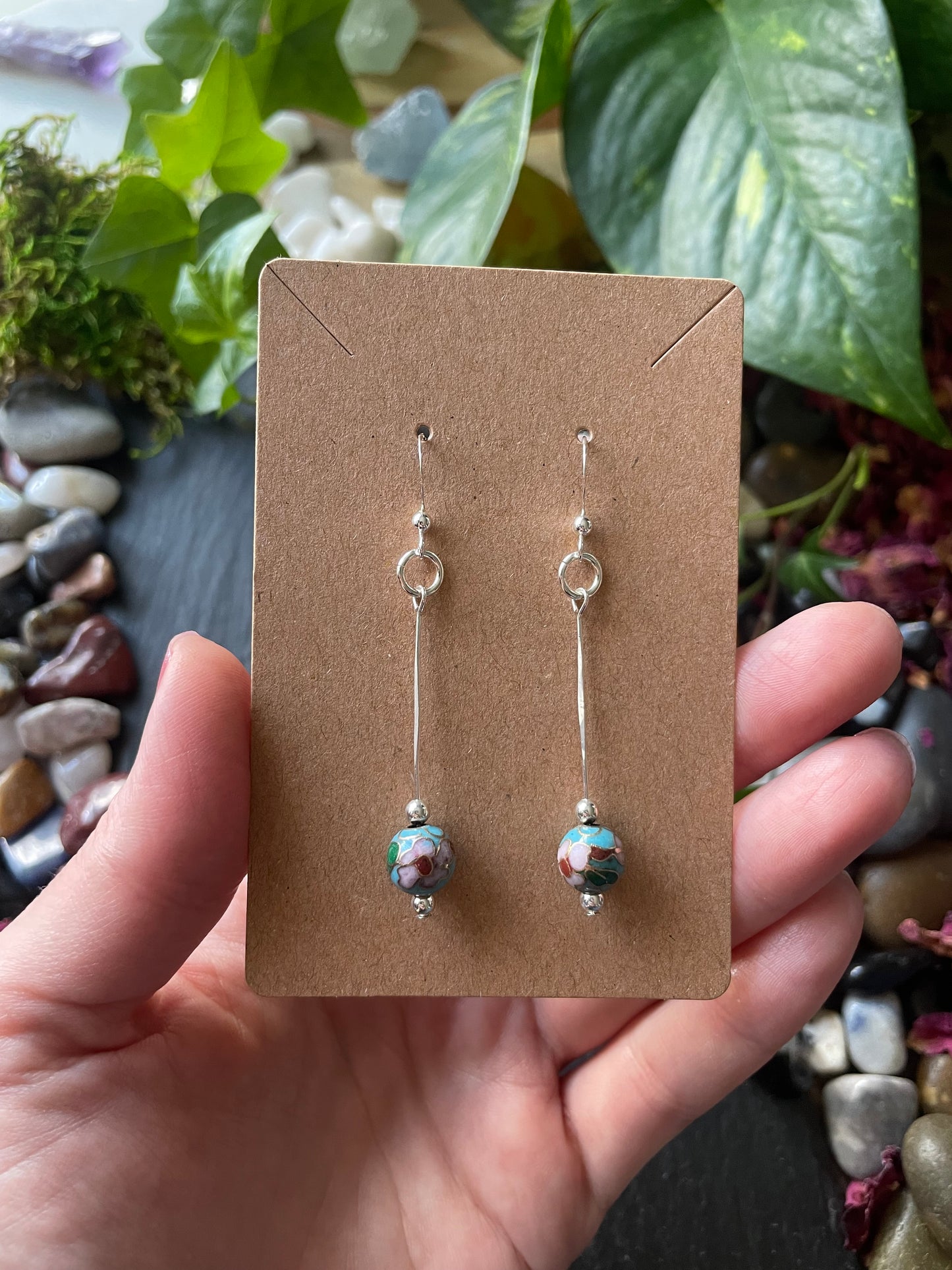 Pair of earrings on a brown card held by a hand with a natural background