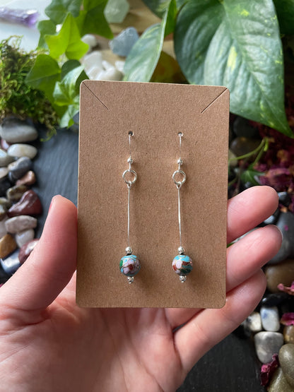 Pair of earrings on a brown card held by a hand with a natural background