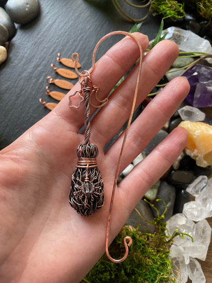 Hand holding a copper wire bookmark with a natural stone and crystal background