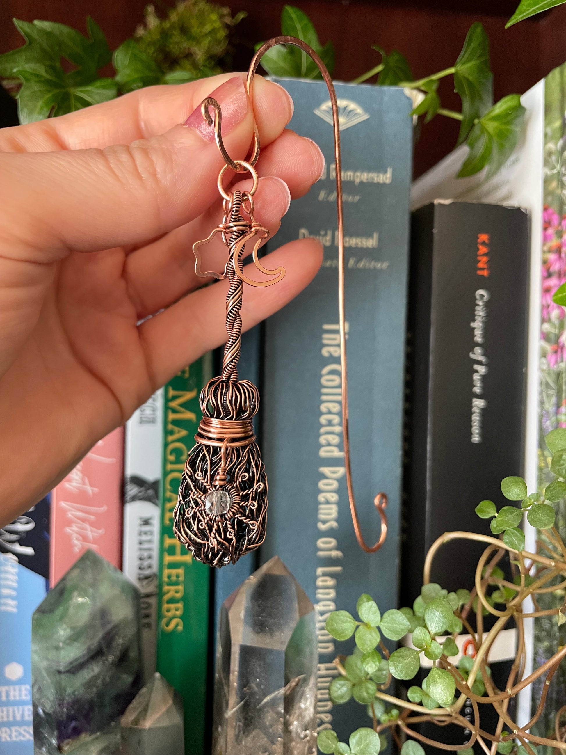 Hand holding a decorative copper bookmark in front of books and plants